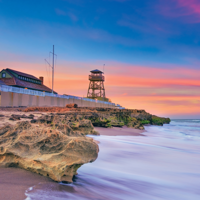 serene beach scene with a watchtower as the waves cascade to the shore at sunset